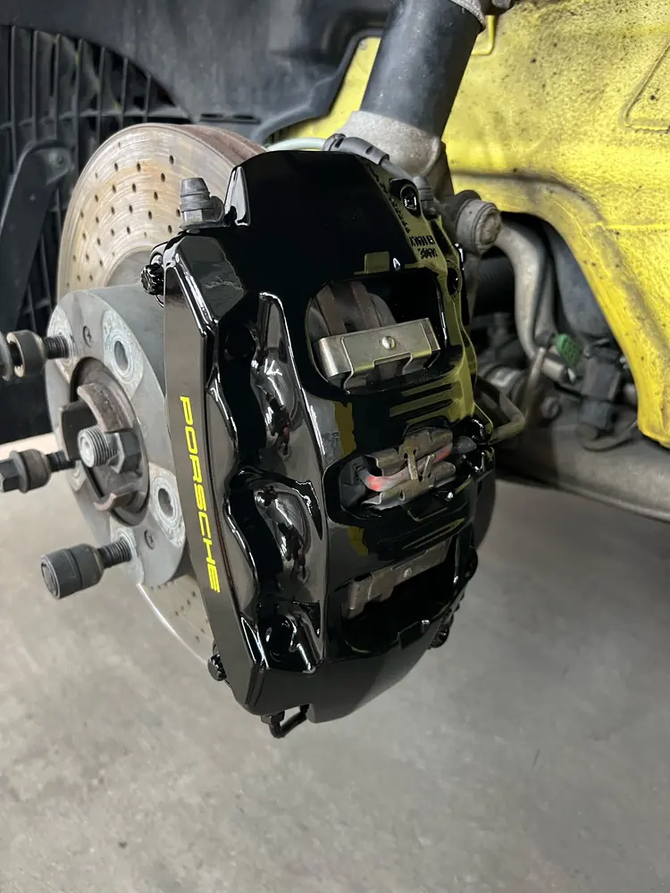 Gloss black Porsche brake caliper and drilled disc after refinishing