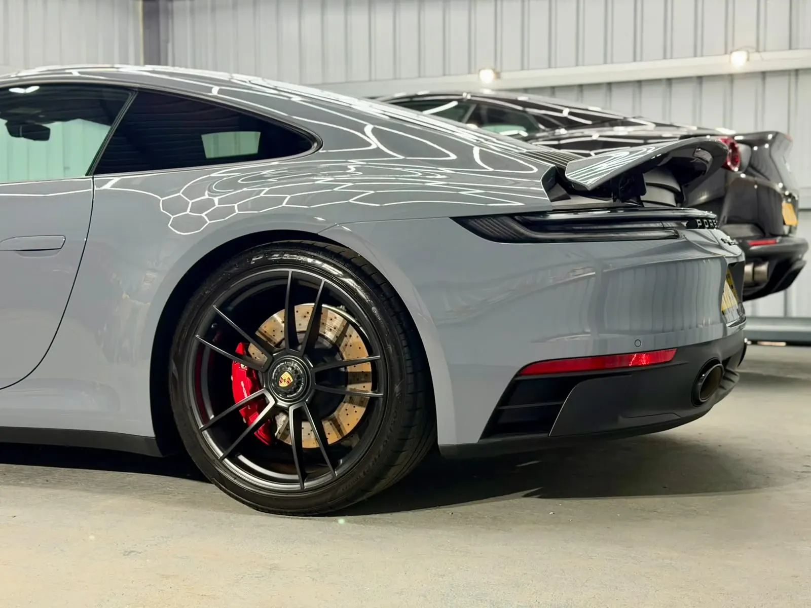 Grey Porsche 911 rear wheel and wing reflecting the hexagonal lights in the Day One Detailing unit